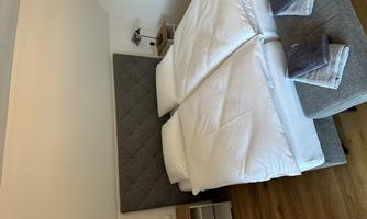 A cozy bedroom with a double bed and bright walls. Next to the bed are nightstands with lamps.