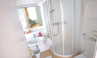 A bright bathroom with a shower, a sink, and a toilet area. There is a window that lets in natural light.