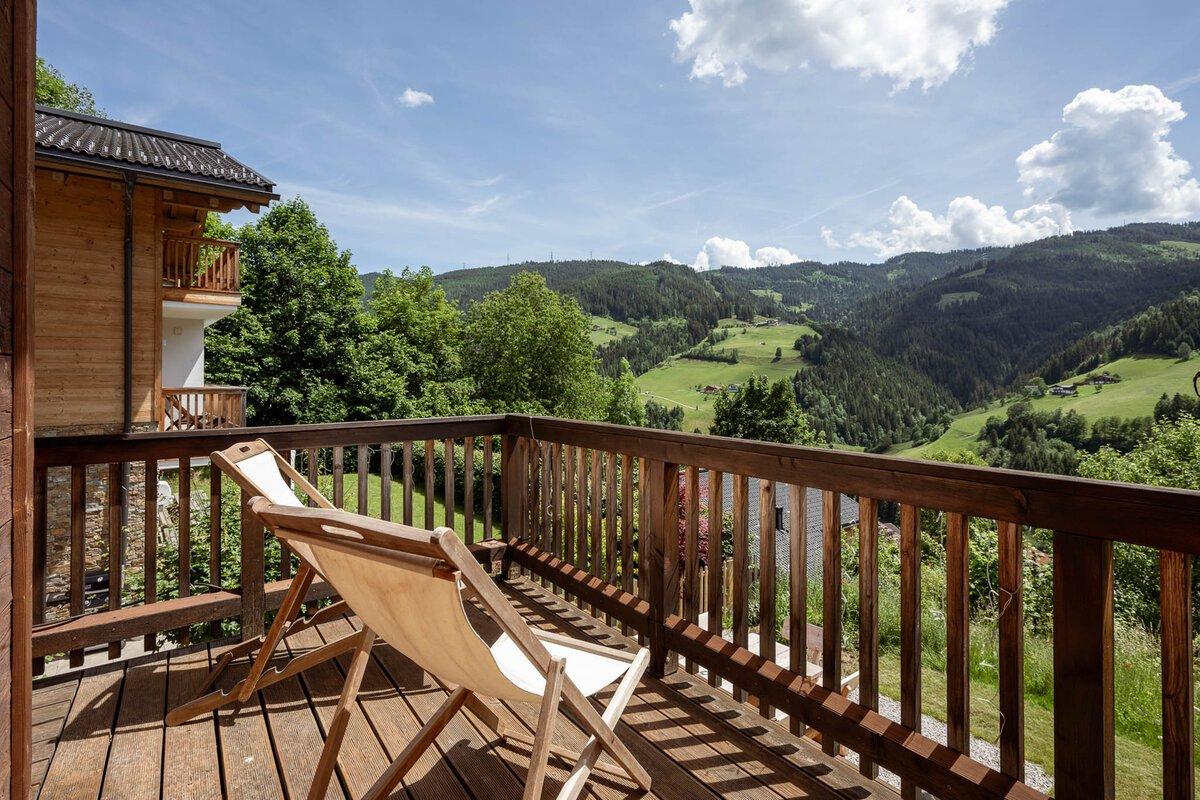 A cozy terrace with a lounge chair and a view of green hills. The sky is clear with a few small clouds.