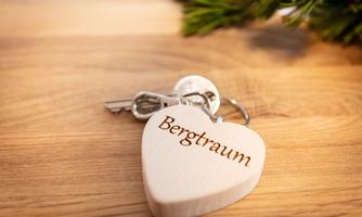A heart pendant with the inscription "Mountain Dream" and a key on a wooden table. Next to it, some green leaves can be seen.