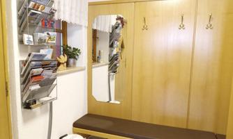 A cozy entrance area with light wooden cabinets and a bench. A mirror and a brochure holder hang on the wall.