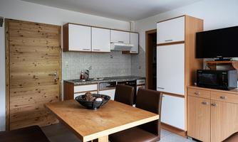 A modern kitchen with wooden shelves and a dining table. The space is bright and functionally furnished.