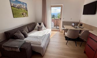 A cozy living room with a sofa bed and a dining table. Large windows offer a view of nature.