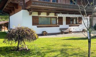 A traditional wooden house in the middle of a green garden. The sun is shining and the sky is blue.