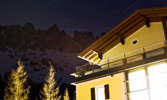 A modern house at night in the mountains. Snow-covered peaks and the starry sky are visible in the background.