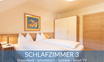 A modern bedroom with a double bed, a desk, and a wardrobe. There is a smart TV and a cozy atmosphere.