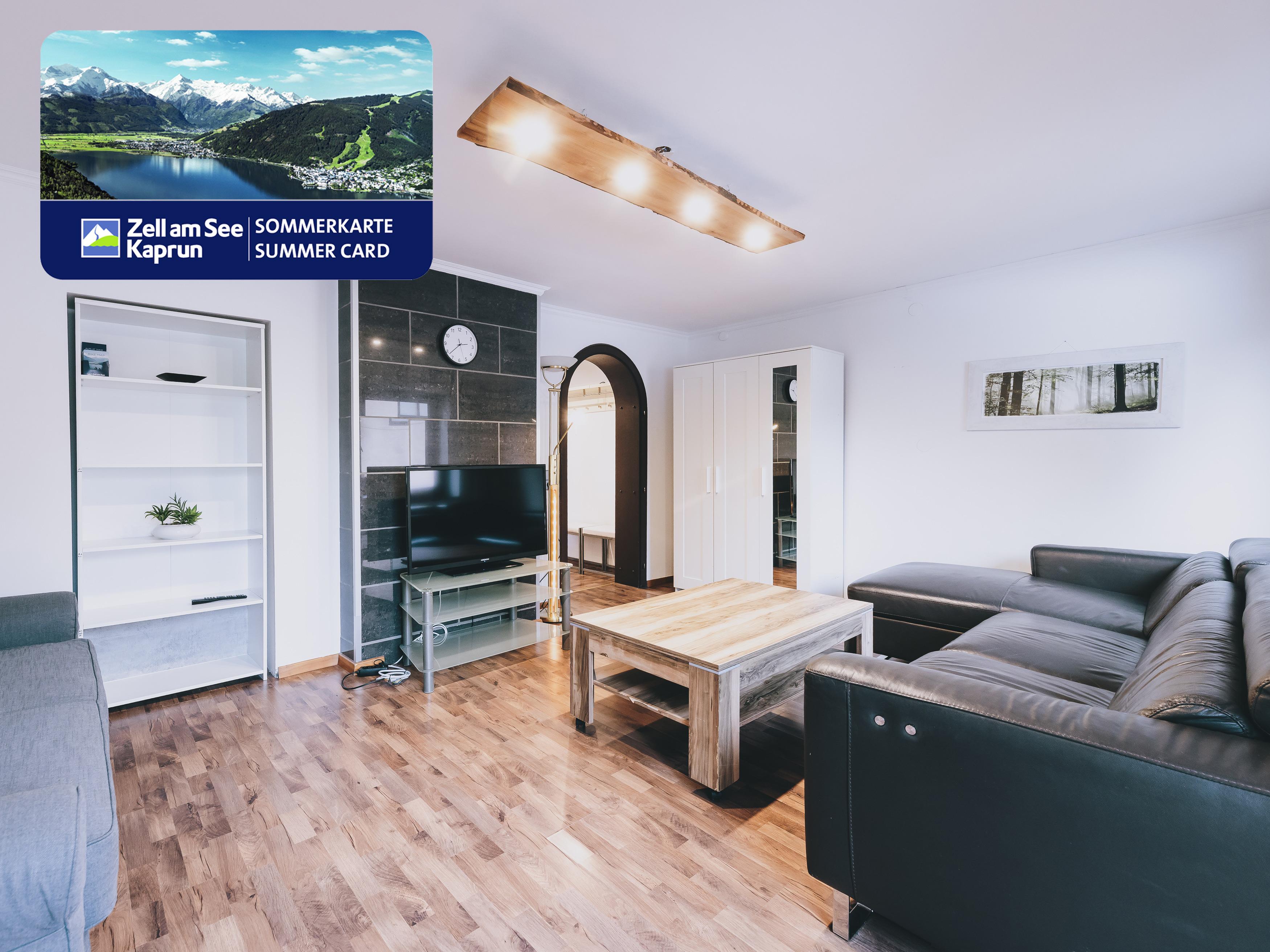 A modern living room with a comfortable sofa and a TV. The room has bright walls and a warm wooden floor.