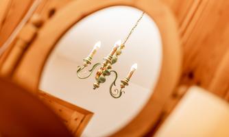An elegant chandelier hangs above a mirror. The mirror reflects the light and creates a warm atmosphere.