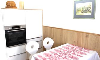 A modern kitchen with a white kitchen cabinet and an oven. The table is covered with a red tablecloth and two chairs have heart-shaped cutouts.