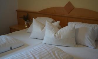 A cozy bedroom with a double bed and many white pillows. The warm tones create an inviting atmosphere.