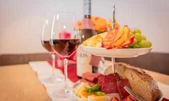 A table set with a selection of delicious foods, including bread, fruits, and sausage. Two wine glasses and a bottle of wine complete the arrangement.