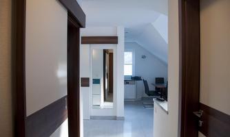 A bright hallway with a large mirror and white walls. In the background, a table and a chair are visible in a cozy room.
