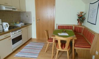 A cozy kitchen with a dining area and wooden chairs. The room is bright and inviting, with a colorful rug and decorative elements.