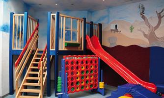 A play area for children with a slide, climbing frame, and a large connect-four game. The walls are brightly colored, creating an inviting atmosphere.