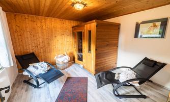 A cozy room with a wooden ceiling and walls. Two lounge chairs and a sauna create a relaxing atmosphere.
