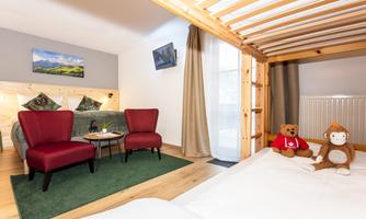 A cozy room with a double bed, red chairs, and a small table. On the floor, there is a carpet and two toys.