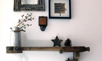 A decorative wall with various pictures and a wooden shelf. On the shelf, there is a vase with flowers and some rustic decorations.