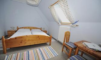A cozy bedroom with two beds and wooden furniture. There is a table and a chair as well as a television on the wall.