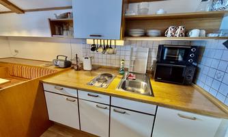 A modern kitchen with wooden shelves and white cabinets. It is well-equipped with a sink, microwave, and dishes.