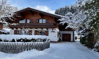 A beautiful wooden house in winter, surrounded by freshly fallen snow. The garden is covered in snow and the trees wear a winter blanket.