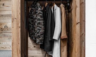 A stylish wooden wardrobe with several hung coats. Below is a black basket.