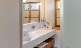 A modern bathroom with a bright vanity and wooden shelves. Large windows provide plenty of daylight.