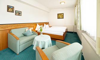 A cozy bedroom with two beds and a seating area. The clear decor and natural light create an inviting atmosphere.