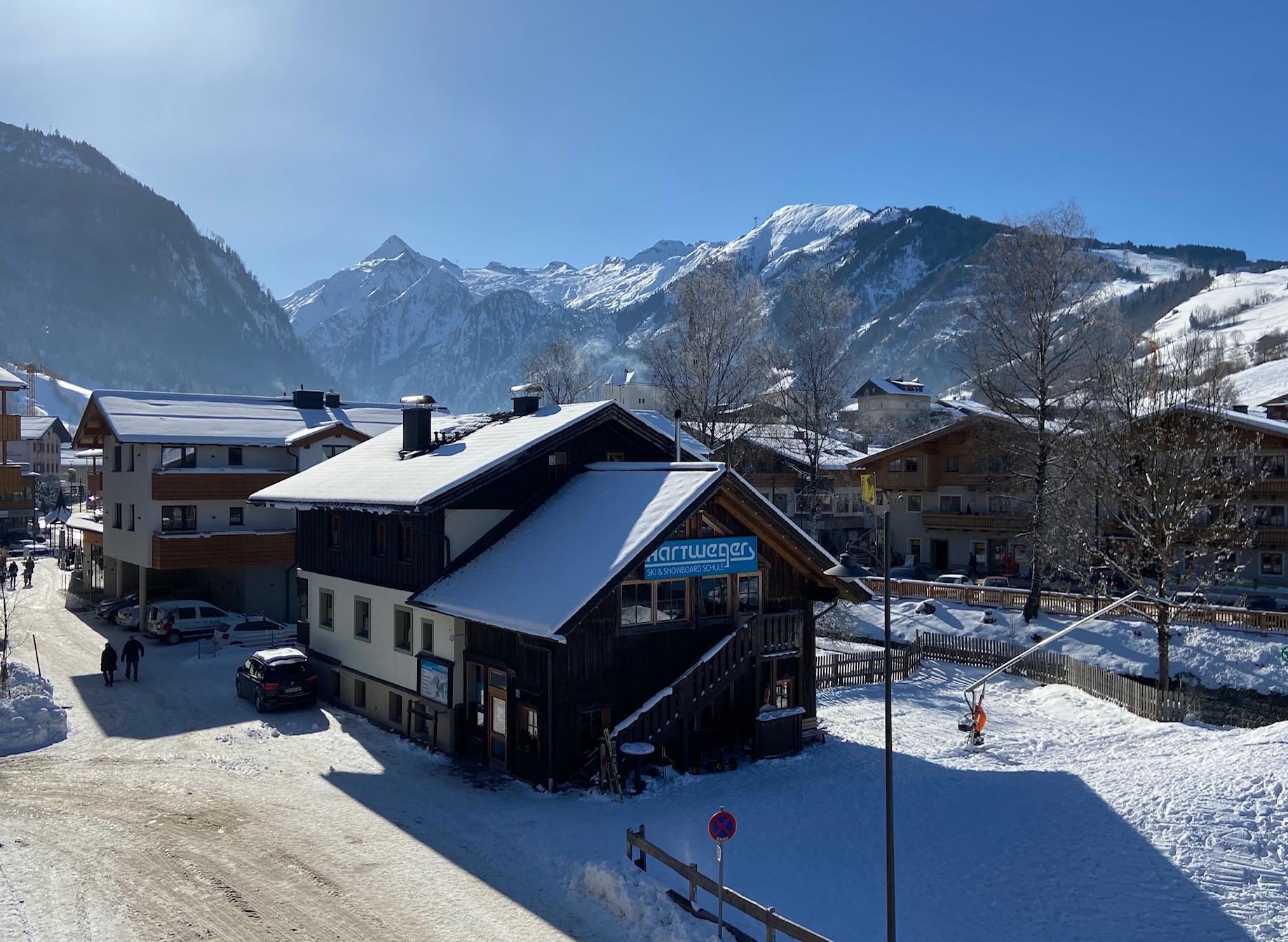 A picturesque winter landscape with snow-covered mountains. In the foreground, a cozy house and a quiet street can be seen.