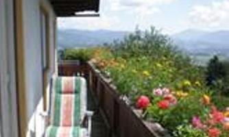 A quiet balcony with two loungers and colorful flowers. In the background, mountains and a blue sky can be seen.