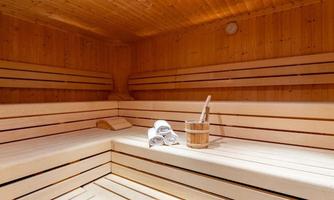 A cozy sauna with wooden benches and soft towels. A bucket with a wooden spoon is ready.