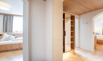 A bright hallway with wooden flooring and modern furnishings. On the left side, a cozy bedroom is visible.