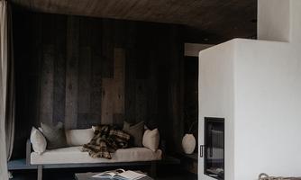 A modern living room with a cozy sofa and a white wall. The room has a dark floor and a small fireplace.