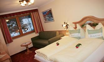 A cozy hotel room with a double bed and a green couch. Large windows offer a view outside and the decor is inviting.