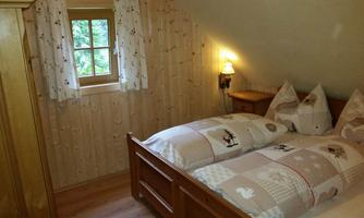 A cozy bedroom with two beds and bright wooden paneling. Next to a window, a warmly glowing lamp radiates an inviting atmosphere.