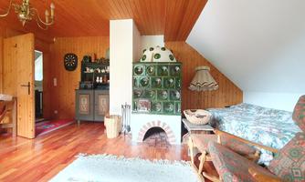 A cozy room with a wooden ceiling and warm wooden floors. There is a traditional stove, a bed, and an armchair in an inviting atmosphere.
