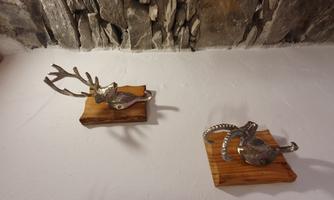 Two decorative wall hooks in the shape of animal heads are attached to a white wall. The hooks consist of a wooden base and metallic animal motifs.