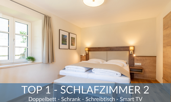 A modern bedroom with a double bed, wardrobe, and desk. The room has large windows and a smart TV.