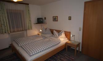 A cozy bedroom with a double bed and checked bedspreads. The room is simply furnished and has a television as well as warm lighting.