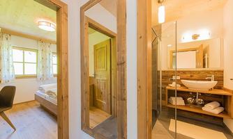 A modern bathroom with a glass shower and a simple sink unit. The room is designed to be bright and welcoming, with wooden details and large windows.