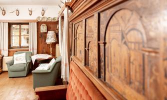 A cozy room with wood-paneled walls and an intricately decorated wall. Two comfortable armchairs and a table create an inviting atmosphere.
