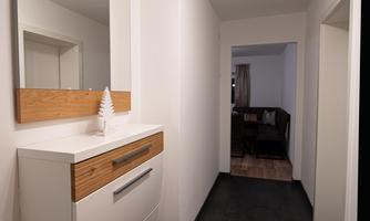 A modern hallway with bright walls and an elegant piece of furniture. A mirror is visible and there is access to another room.