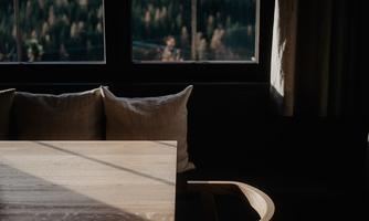 A minimalist room with a wooden table and cozy cushions. Soft light falls through the window onto the furniture and the natural surroundings.