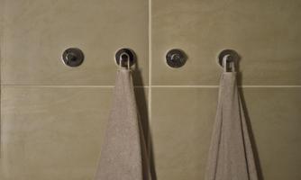 Two towels hang on walls with a smooth, beige tile pattern. The hangers are made of metal and create a modern look.
