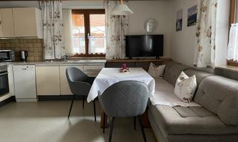 A modern kitchen with a dining area and a cozy couch. The room is bright and friendly with large windows.