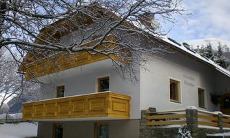 A charming house in winter with a wooden balcony. The garden is covered in snow and the trees are lightly dusted with snow.