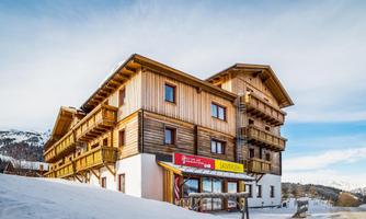 A modern wooden house in the snow, surrounded by mountains. The facade is designed to be friendly and inviting.