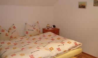 A cozy bedroom with a large bed and colorful pillows. The walls are light and there is a nightstand with a lamp.