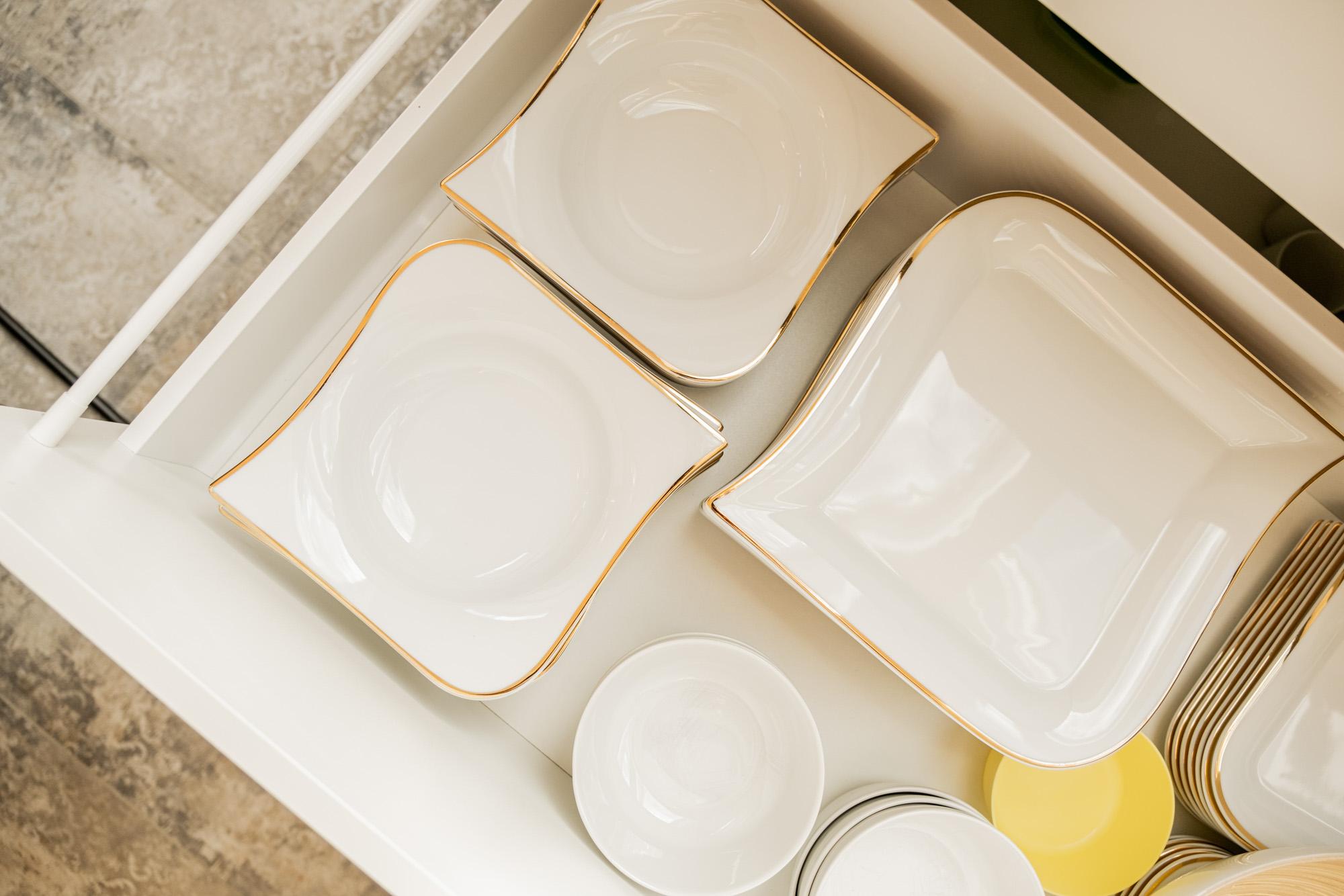 A drawer with elegant dishware. Inside are various plates and bowls in white with golden edges.