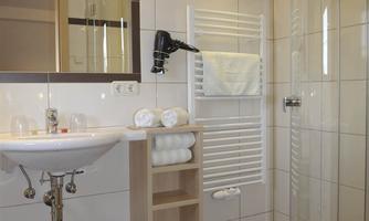 A modern bathroom with a glass shower and a sink. White tiled walls and wooden details create a bright, inviting atmosphere.