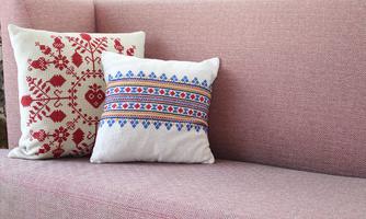 Two decorative cushions on a pink sofa. One has a red floral pattern and the other has a colorful geometric design.
